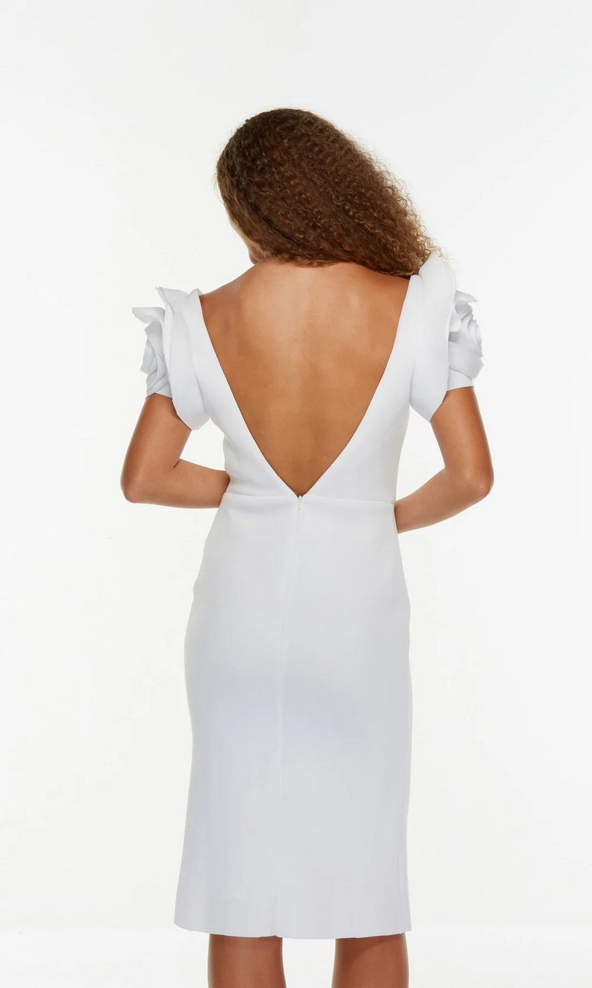 A woman with curly hair models the Alyce 70024 knee length white party dress, which has ruffled short sleeves and a deep V-back, standing against a plain white background.